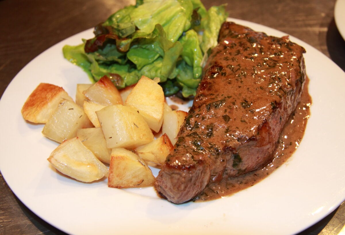Steak with sauce bordelaise served on a white plate with roasted rosemary potatoes and salad.