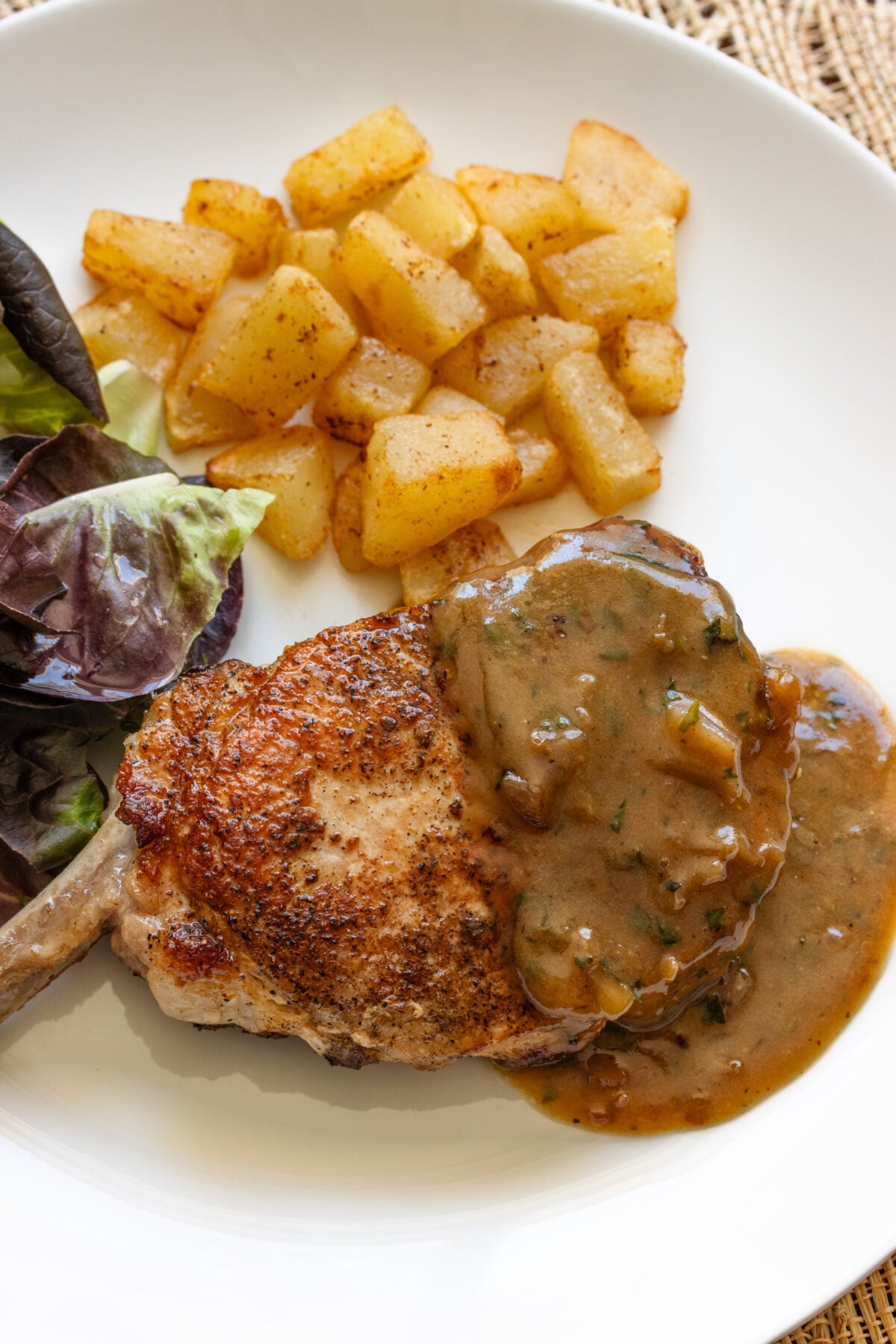 White serving plate with the pork chops and beer and mustrd gravy over it and potatoes alongside.