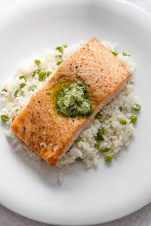 Salmon with Beurre Maitre d'Hotel served on a bed of butter rice with peas, on a white round plate.
