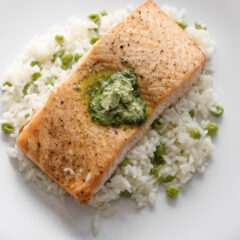 Salmon with Beurre Maitre d'Hotel served on a bed of butter rice with peas, on a white round plate.