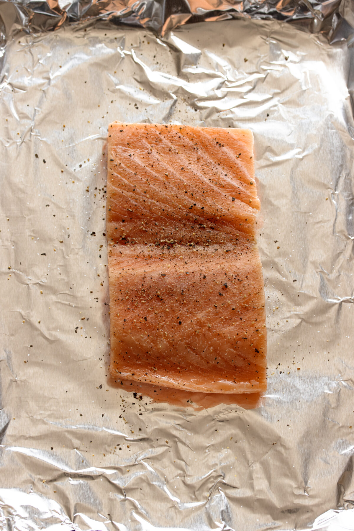 Salmon placed over aluminum foil in a baking sheet.