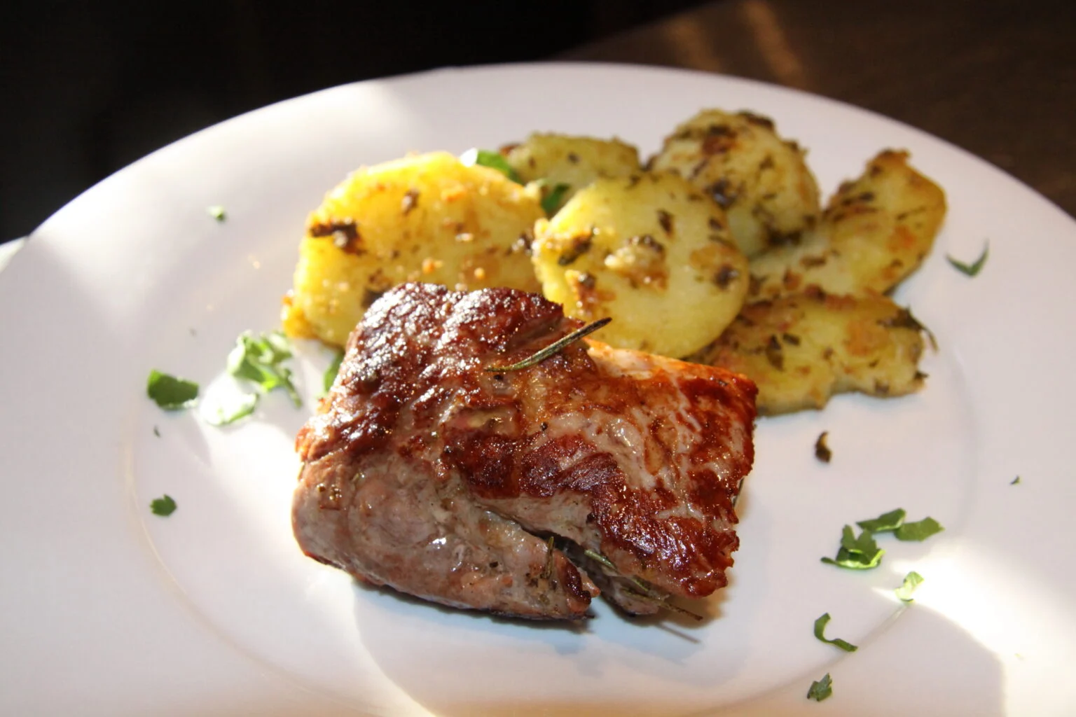 The finished pan seared pork tenderloin recipe served with potatoes on a white plate.
