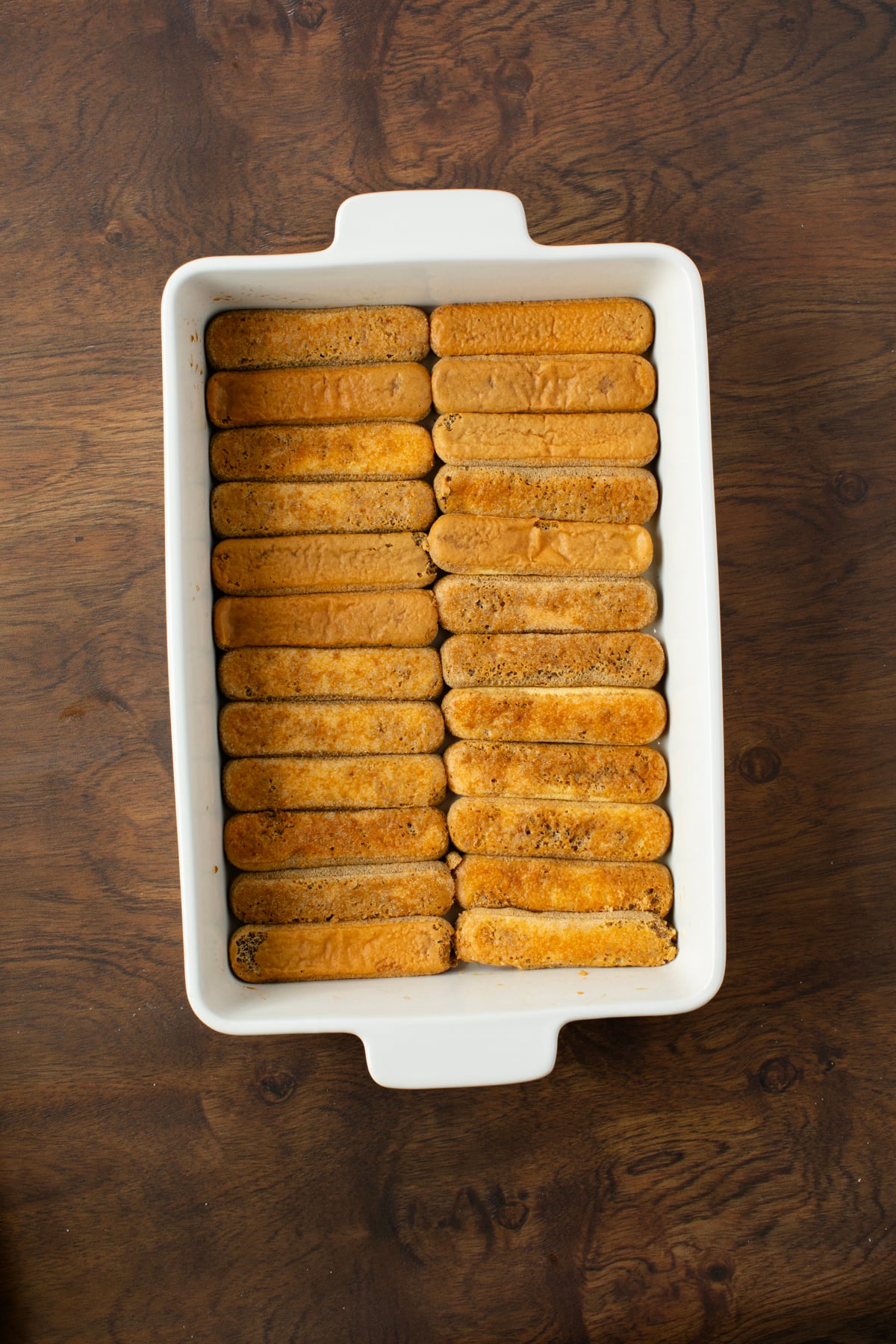 Layer of coffee dipped savoiardi is placed into the bottom of a baking dish.