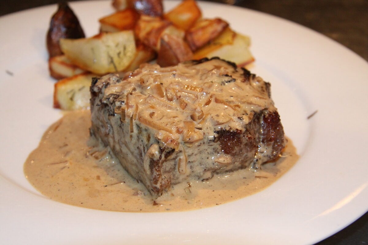Close up to the pan seared New York steak with whiskey cream served on a white plate.