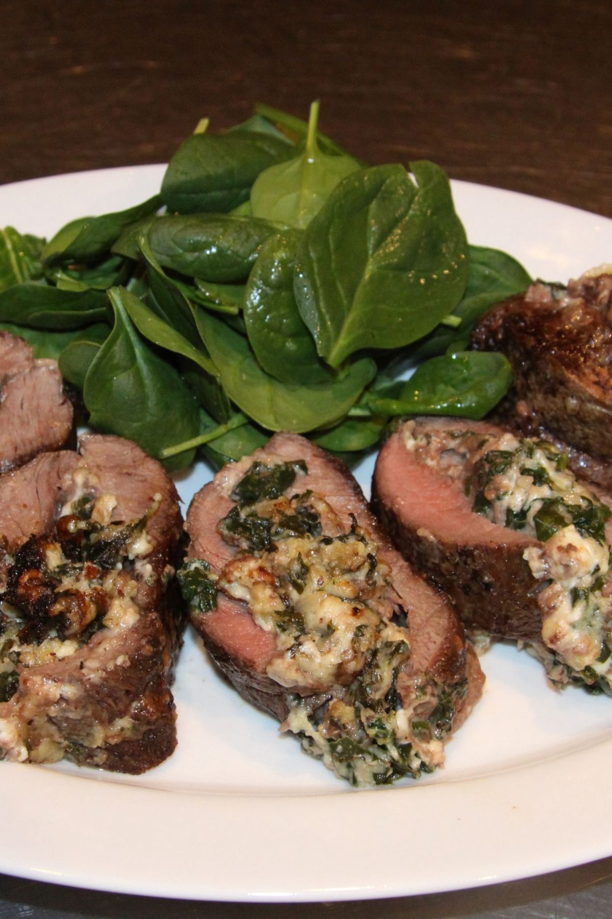 Spinach and gorgonzola stuffed flank steak sliced and placed on a white plate.