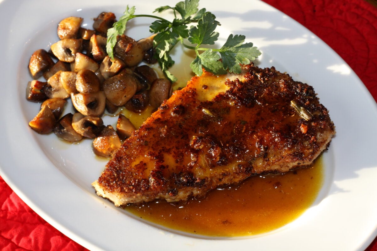 Swordfish with orange caramel sauce served with mushrooms on a white plate