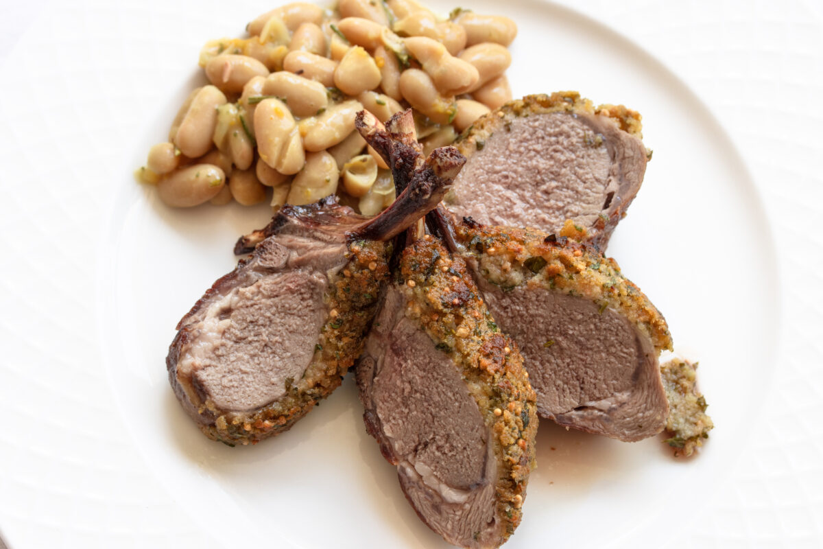 Sliced Herb-crusted rack of lamb with white bean rosemary ragout on a white plate.