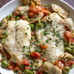 Cod Piccata with Artichokes, Tomatoes and Olives served in a round white dish.