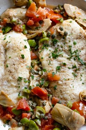 Cod Piccata with Artichokes, Tomatoes and Olives served in a round white dish.