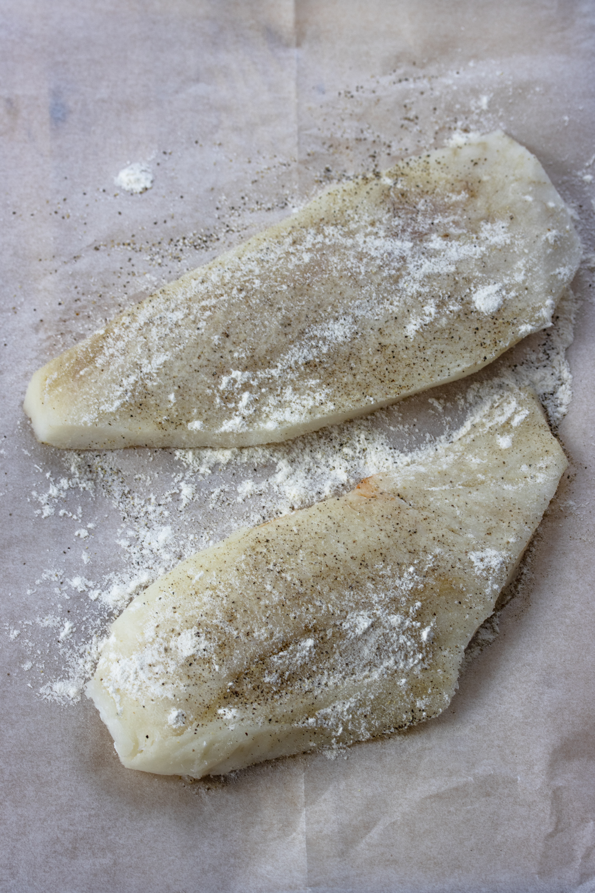 Cod sesoned with salt and pepper adn dredged in flour on a parchment paper. 