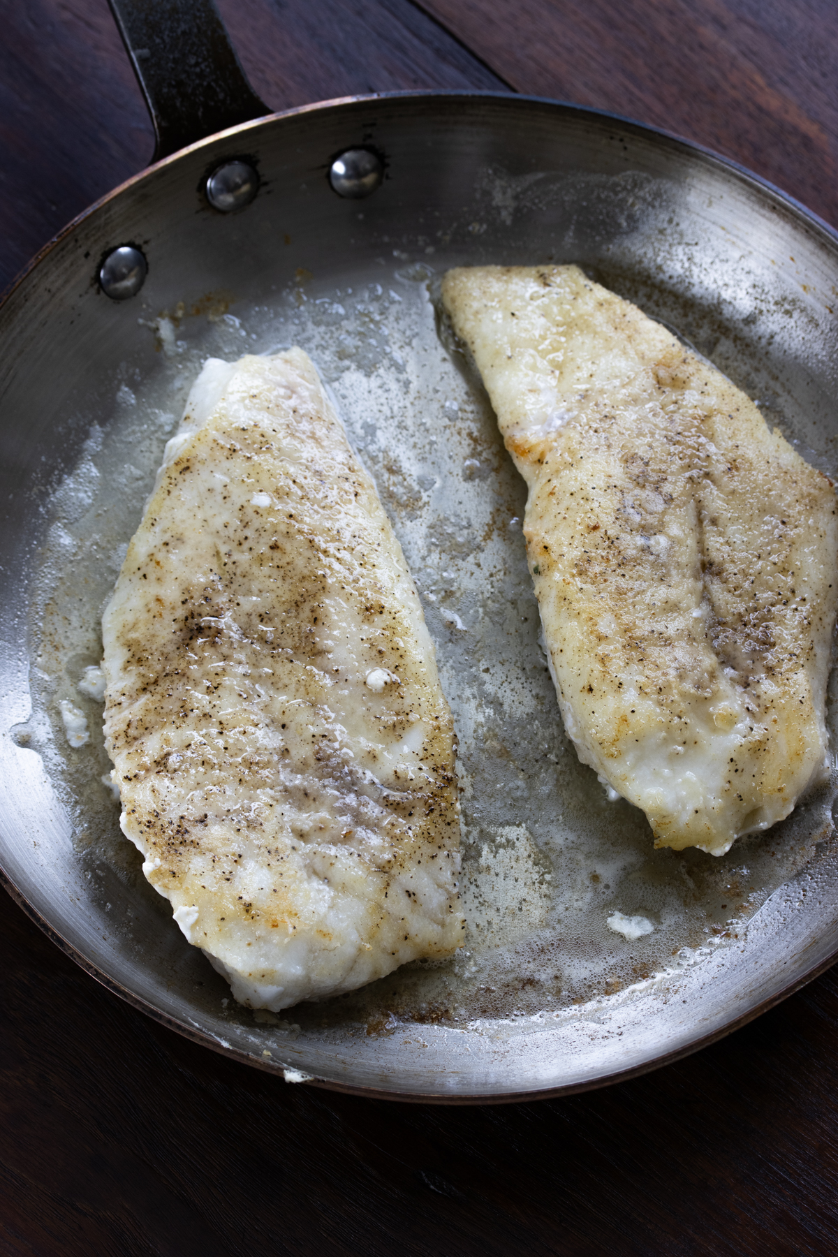 Cod cooking in a large skillet with butter until crispy. 