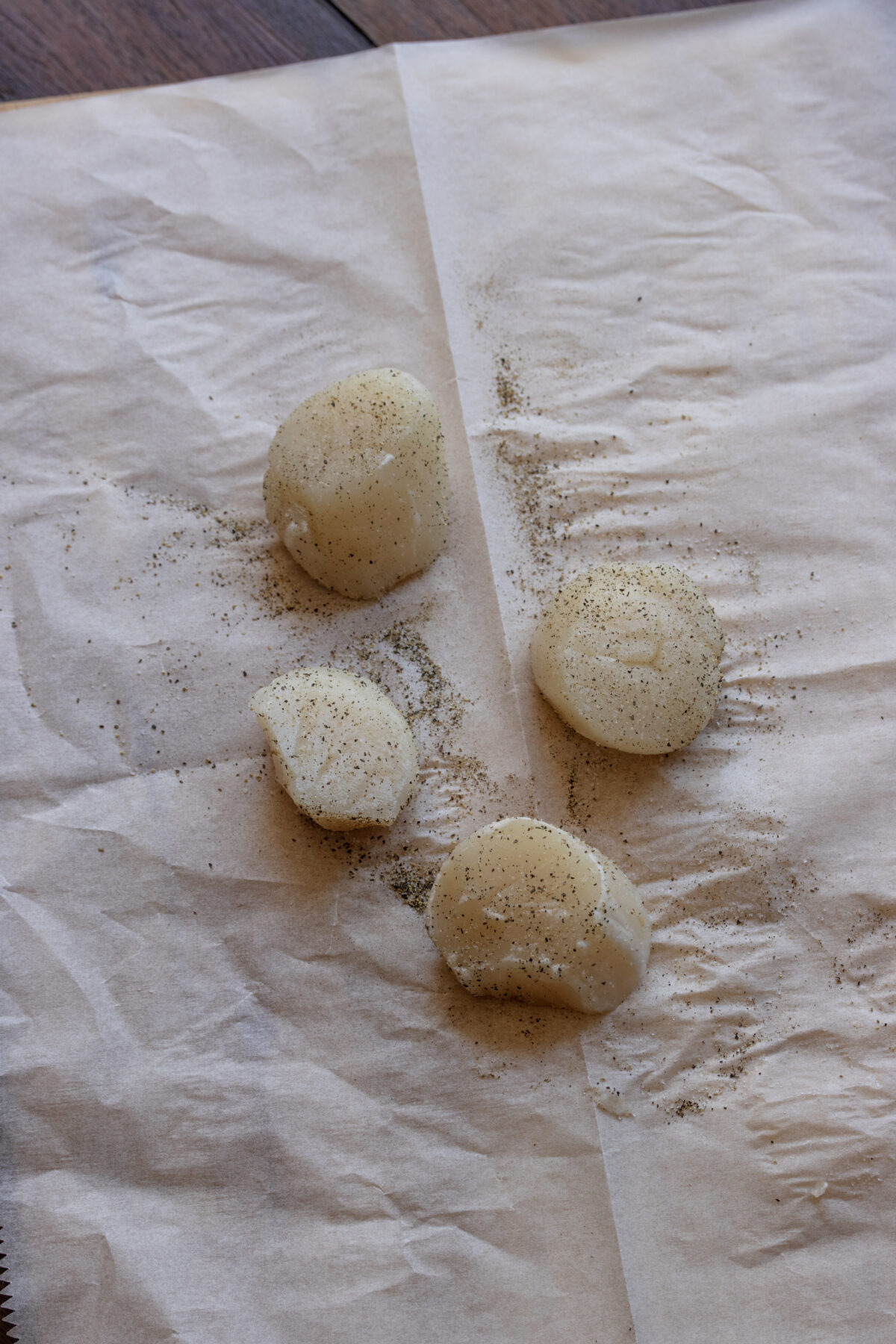 Scallops seasoned with salt and pepper on a parchment paper.