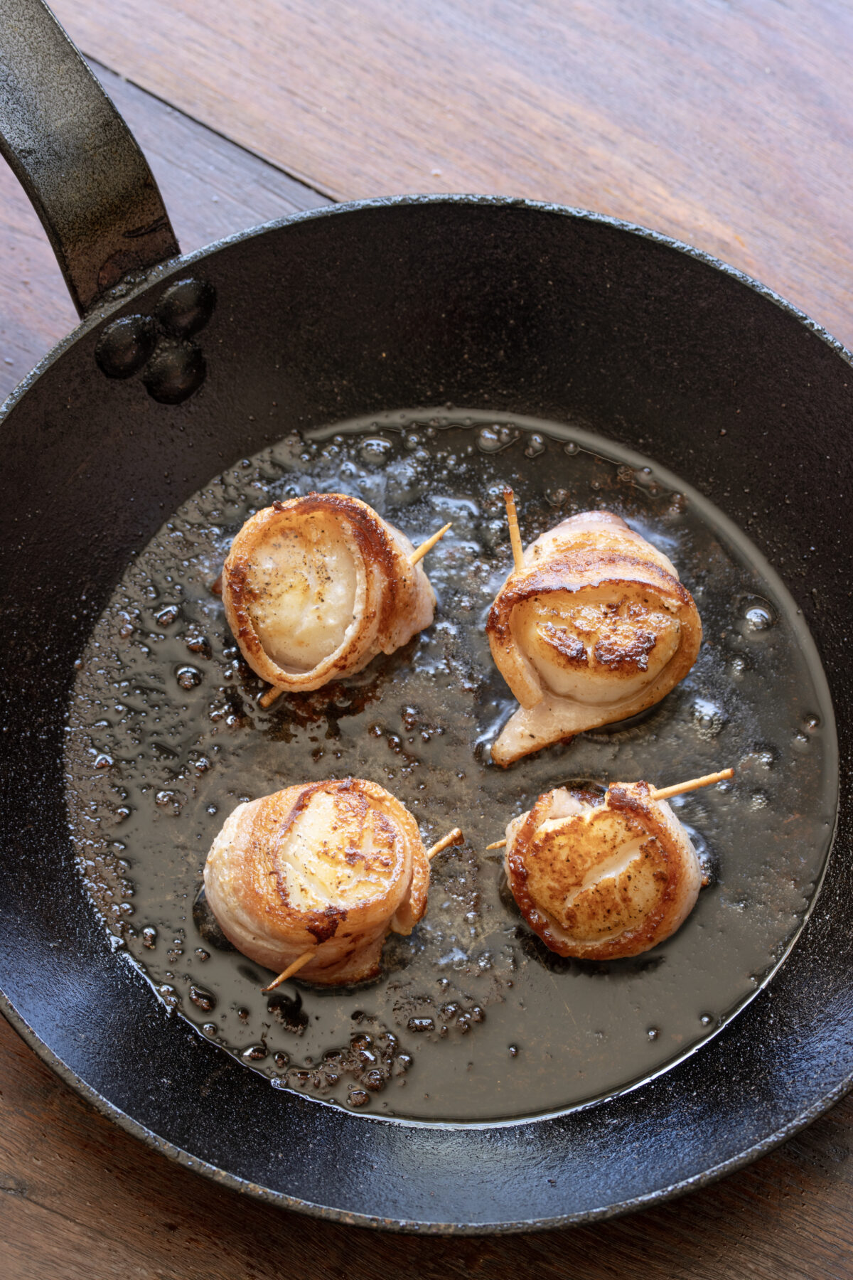 Scallops wrapped with bacon cooked in skillet.