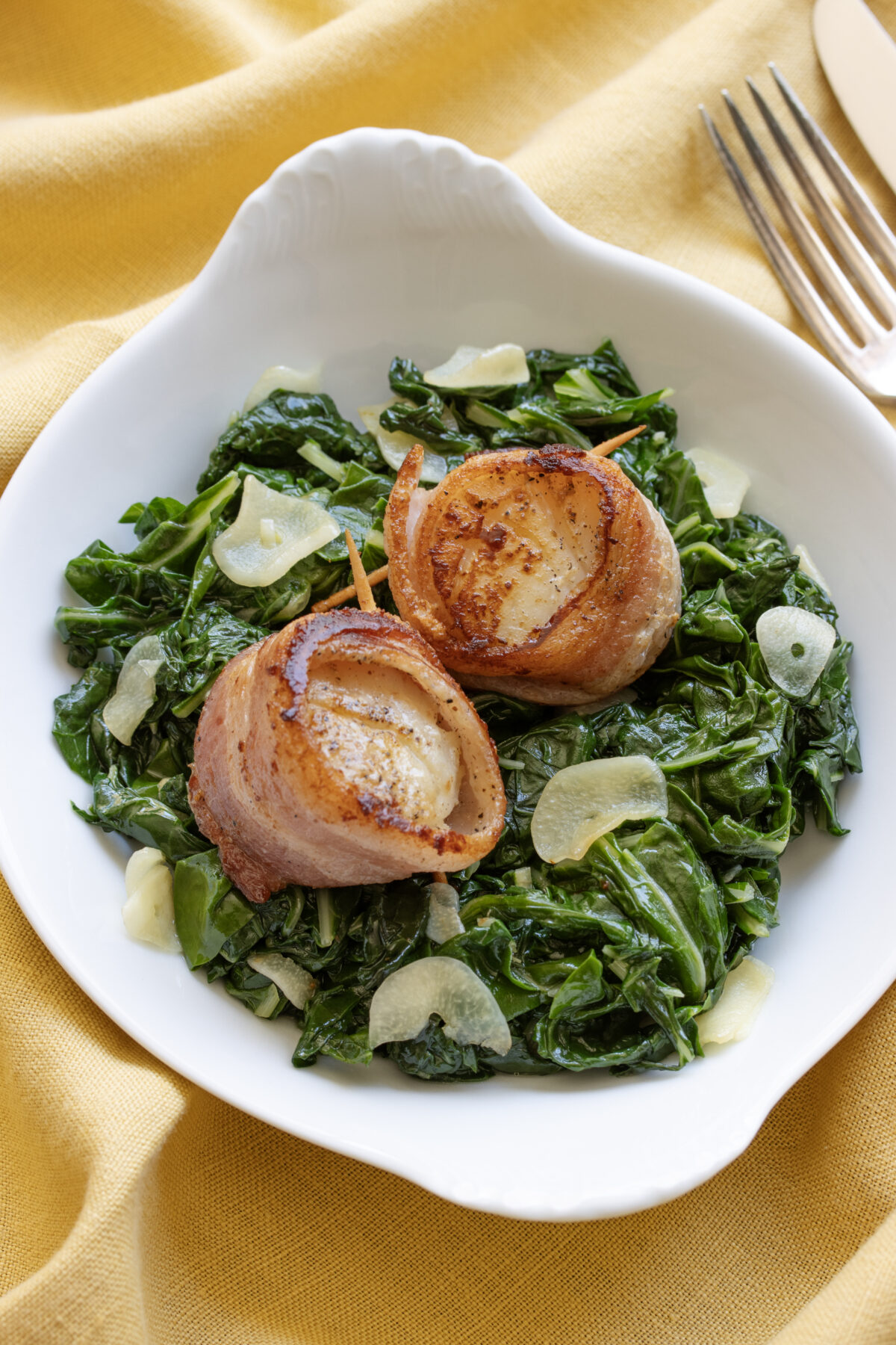 Bacon Wrapped Scallops with Swiss Chard served on a white plate.