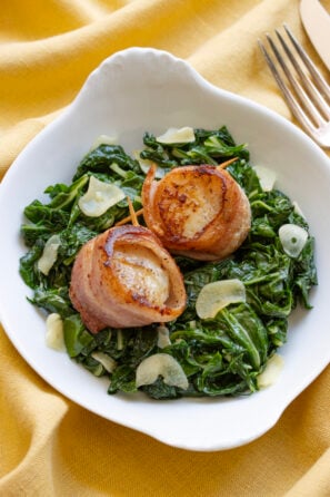Bacon Wrapped Scallops with Garlic Swiss Chard on a white plate