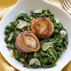 Bacon Wrapped Scallops with Garlic Swiss Chard on a white plate