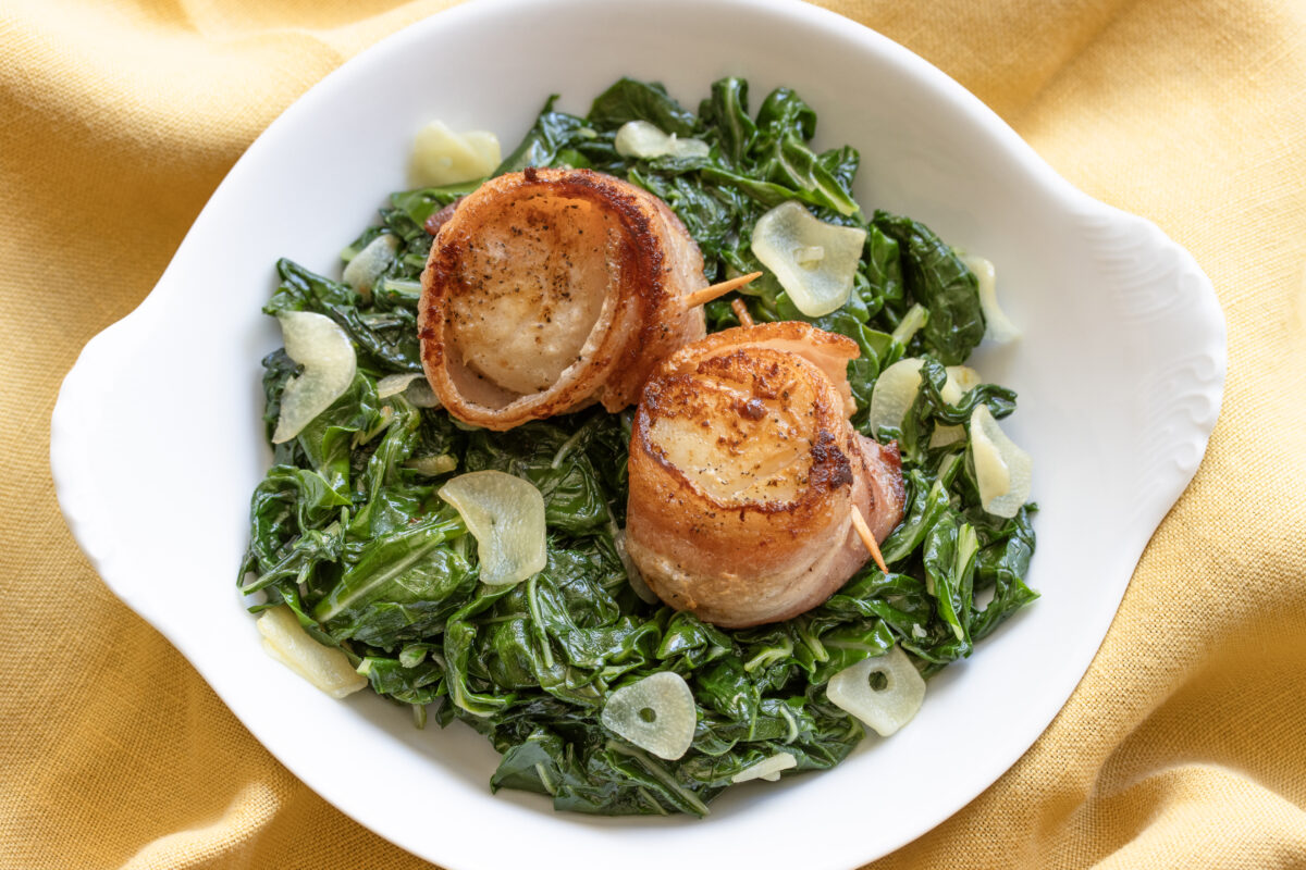 Two scallops sitting on a bed of Swiss chard.