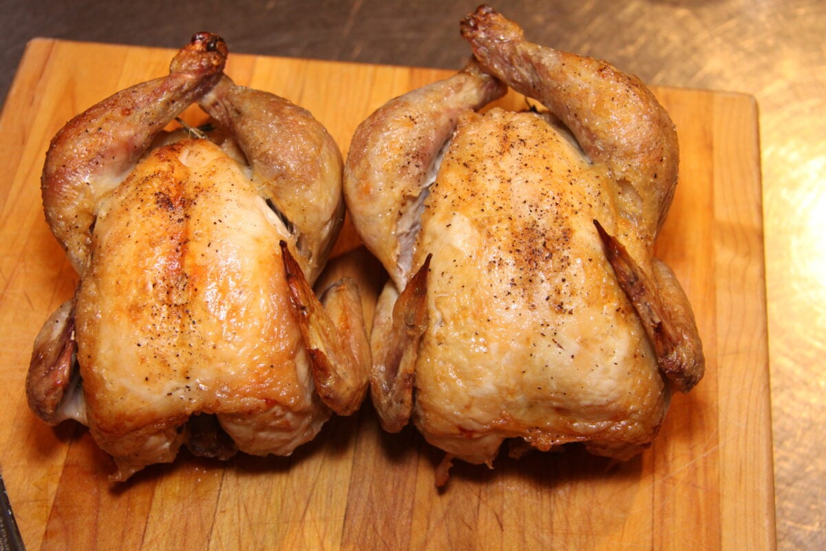 Cornish game hen cooked and sitting on a cutting board before being cut in half.