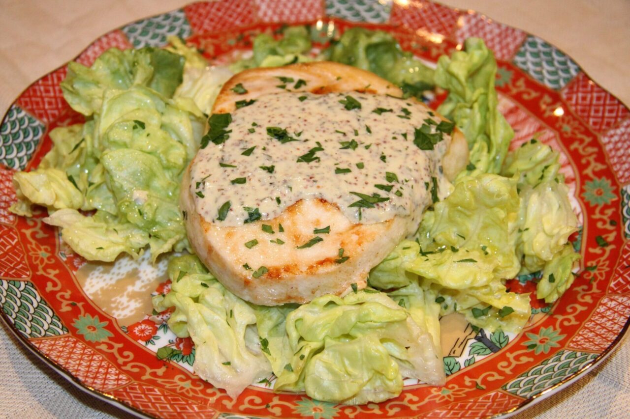 Swordfish steak served with dijon sauce over it and sitting on a lettuce bed.