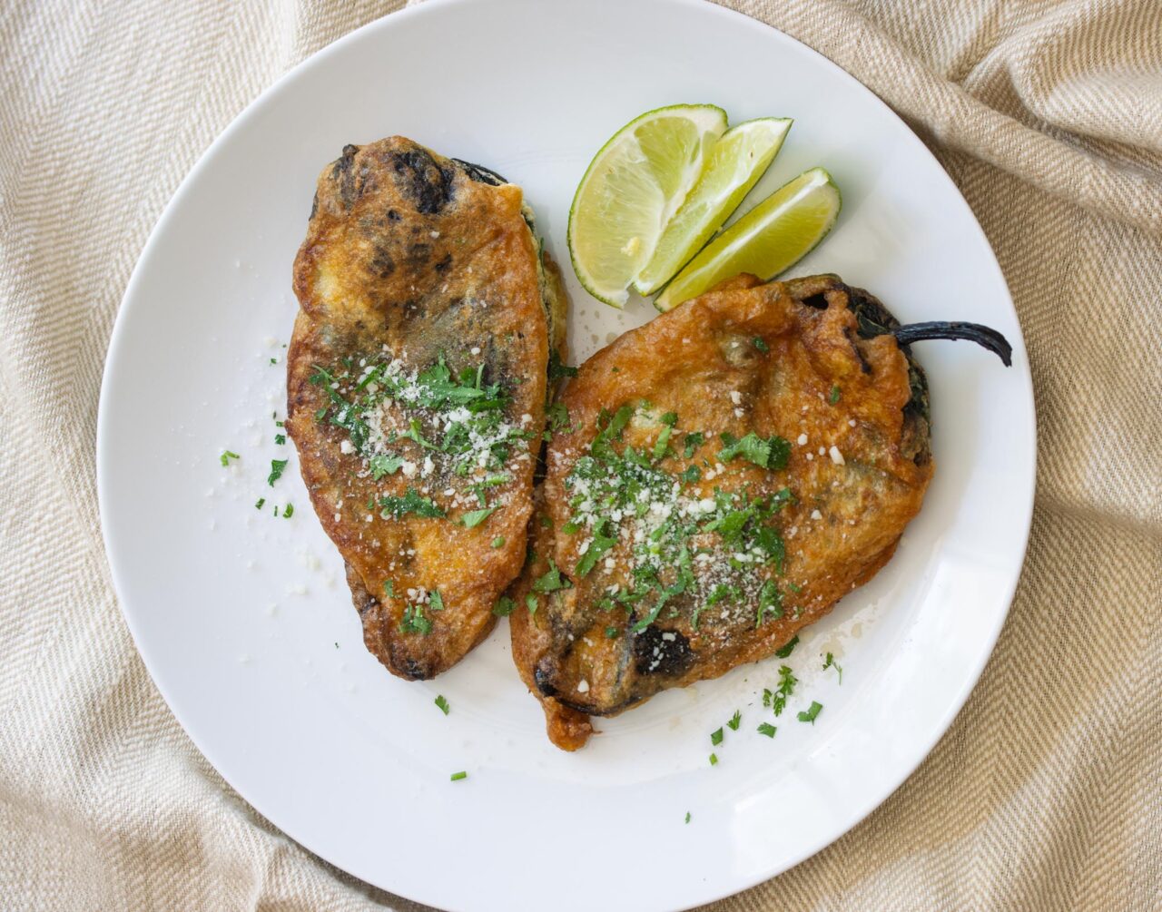 Chiles Rellenos Rellenos two on a serving plate with lime wedges.