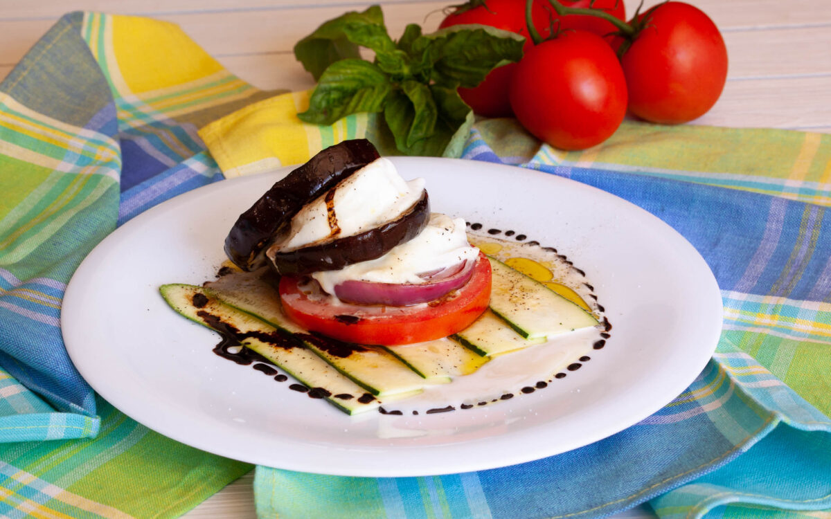 Grilled Vegetables Stack served on a white plate surrounded by fresh tomatoes and basil