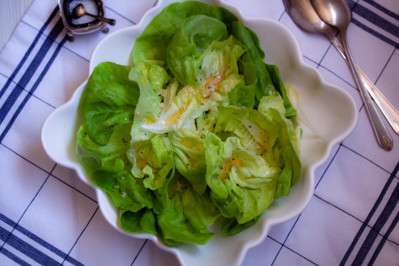 The salad in a white bowl with spoons in the background.