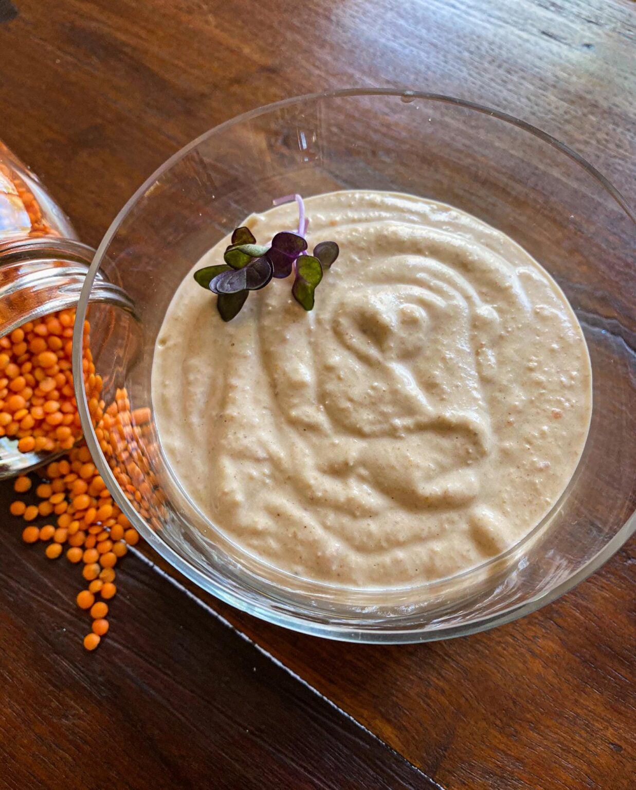 Finished lentil hummus served in a glass bowl. Lose red crimson lentils surrounding it for decoration. 