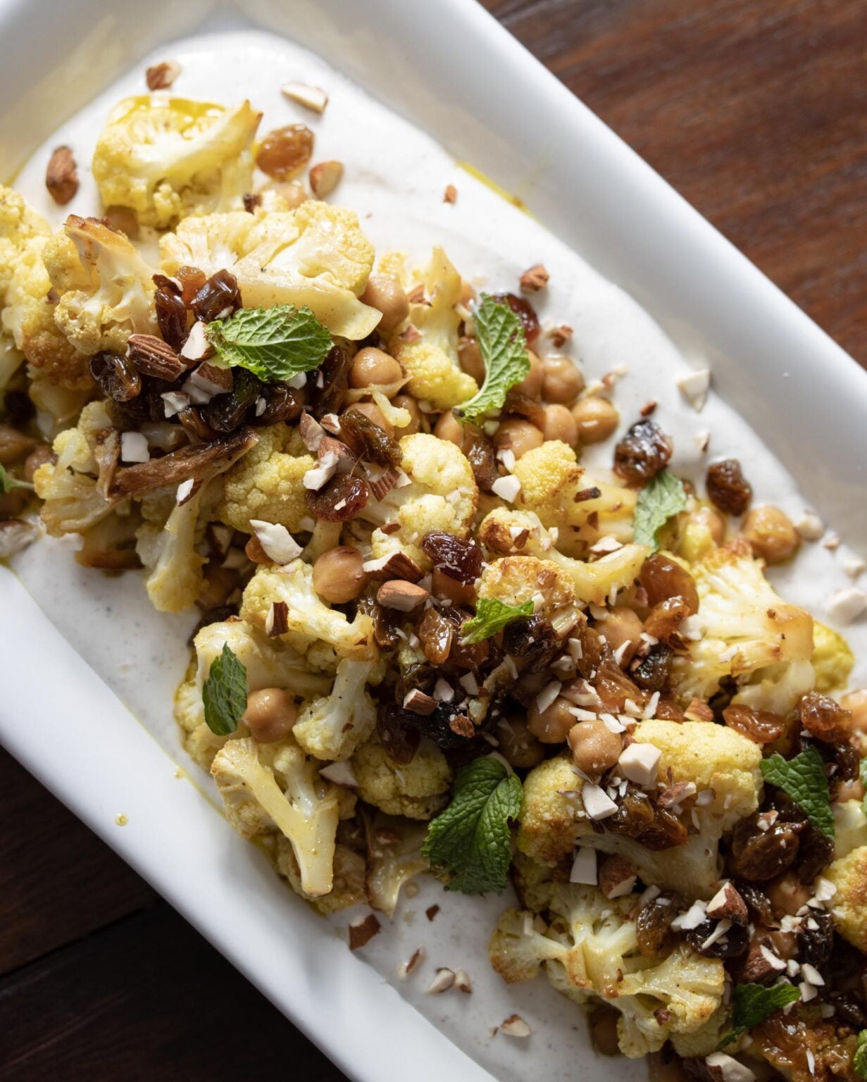 Cauliflower curry recipe seasoned with curry vinaigrette sits over a bed of spiced yogurt on a white rectangular plate. 