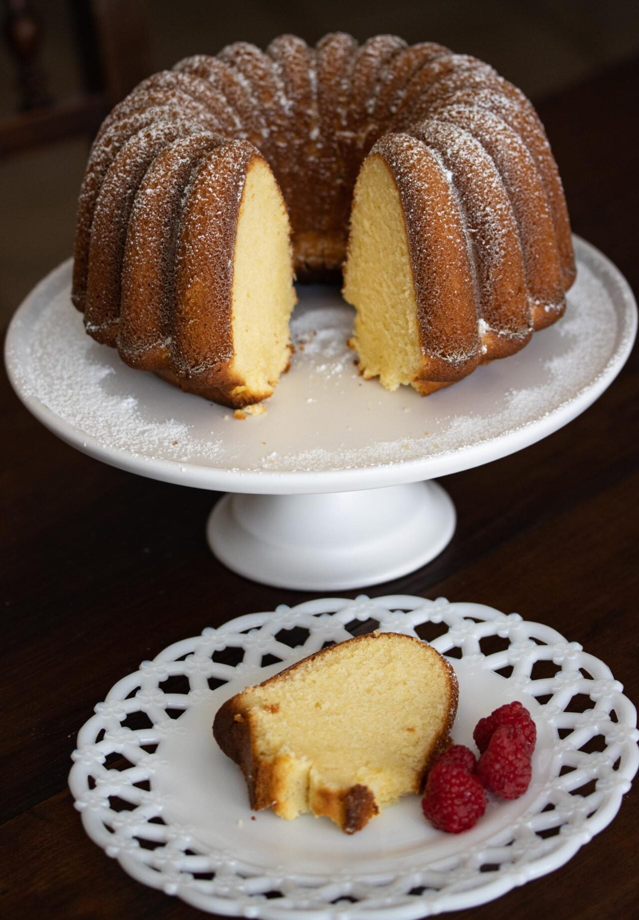 Lemon Pound Cake Lemon Pound Cake on a white cake stand and a slice served on a white dish with raspberries
