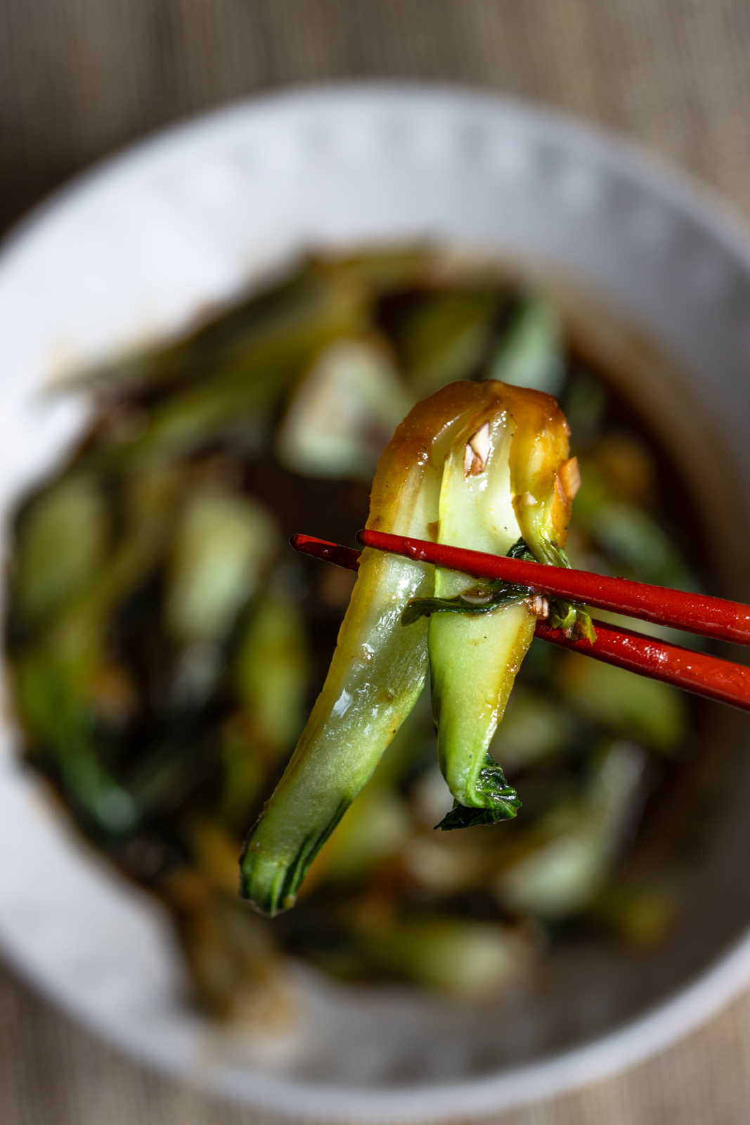 Close up of cooked steamed bok choy helod by red chop sticks.