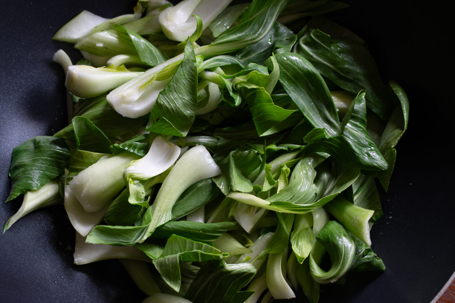 Bok choy added to the garlic and ginger cooing in a wok. 