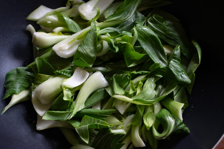 Bok choy added to the garlic and ginger cooing in a wok.
