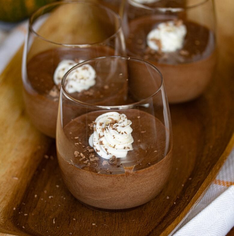 Chocolate dulce de leche in a short glass container standing over a wooden tray.