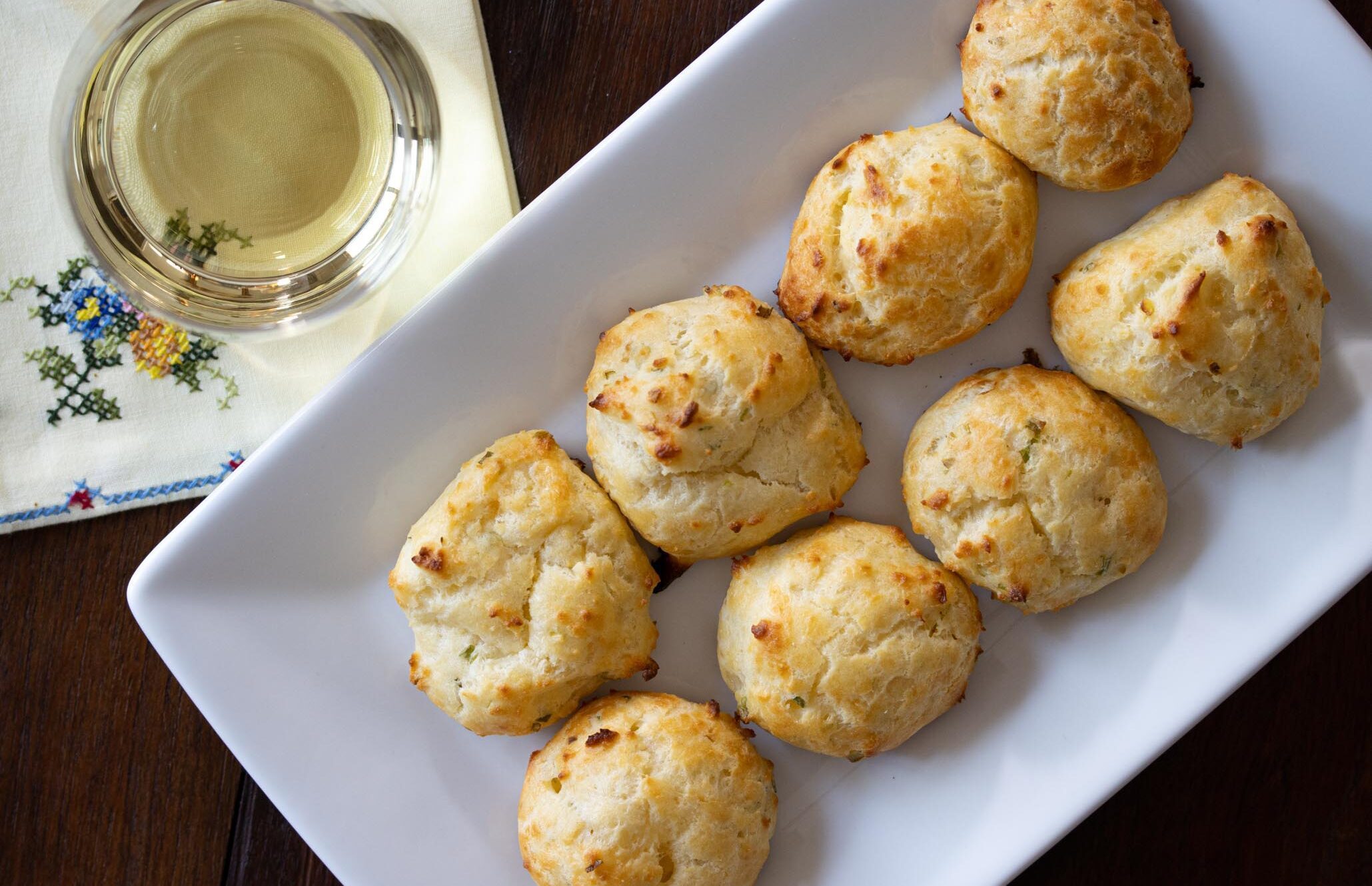 Gougeres with cheese and scallions on a white rectangular plate and a glass of white wine