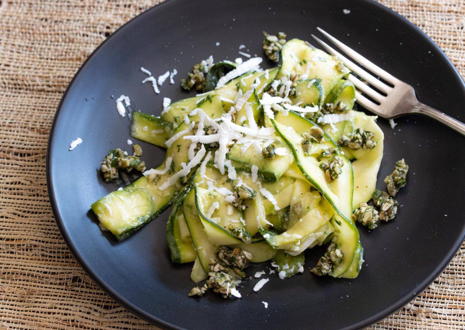 zucchini salad with avocado, pepita parsley gremolata in a black serving plate