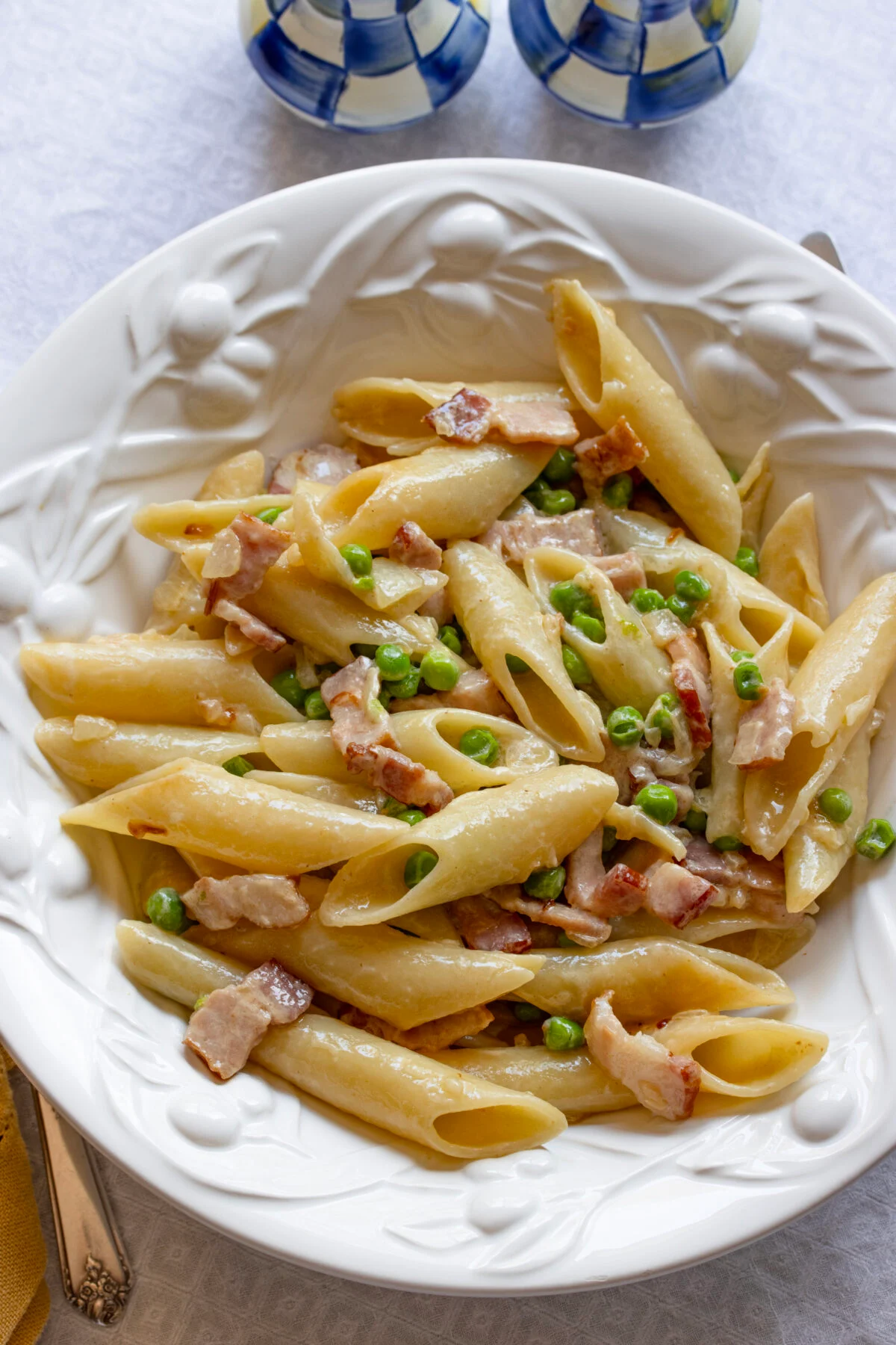 penne pasta, peas and bacon Creamy penne pasta with peas and bacon served on a white ceramic decorated plate.