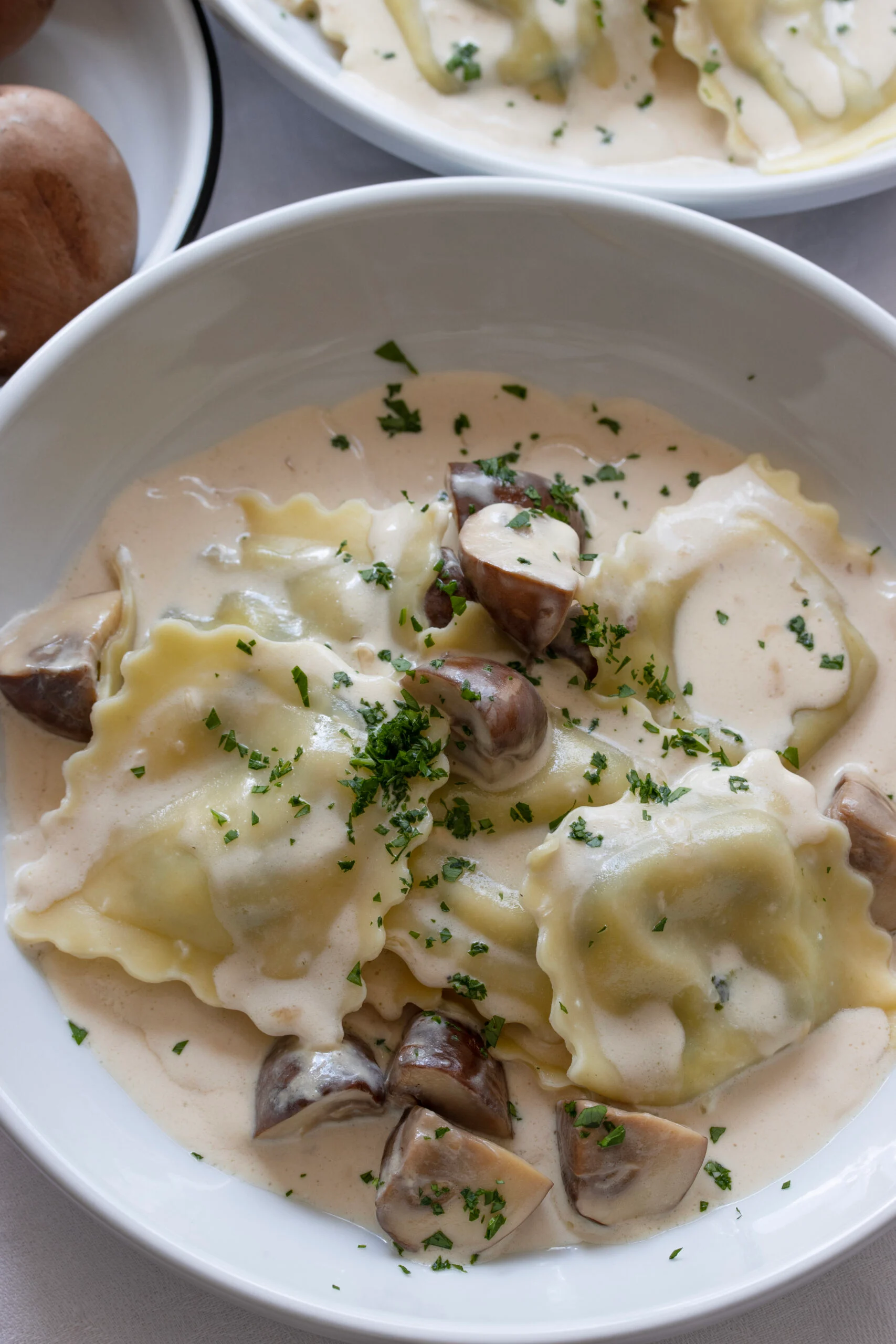 Ravioli with Creamy Mushroom Sauce served in a white soup bowl with sprinkled parsley over it.