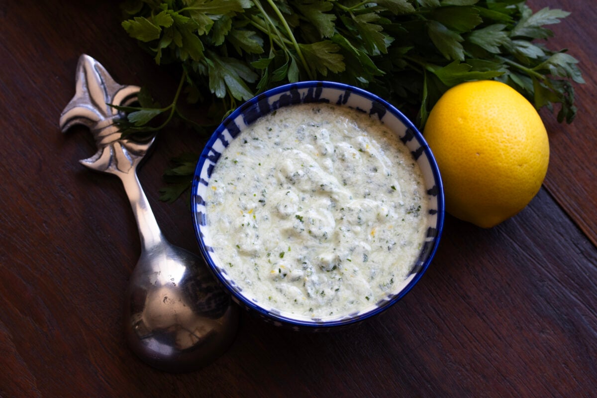 Yogurt feta sauce in a small blue bowl with a serving spoon next to it.