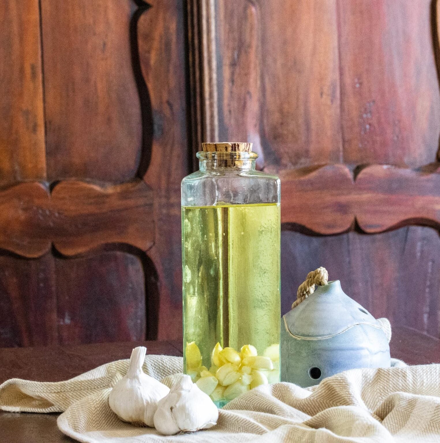 Garlic Olive Oil A glass bottle of the oil on the table with raw garlic next to it.