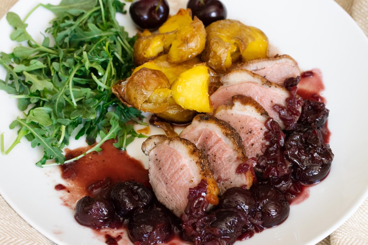Duck Breast with Port and Cherry Sauce A plate with duck and cherry sauce with port wine reduction, potatoes and salad.