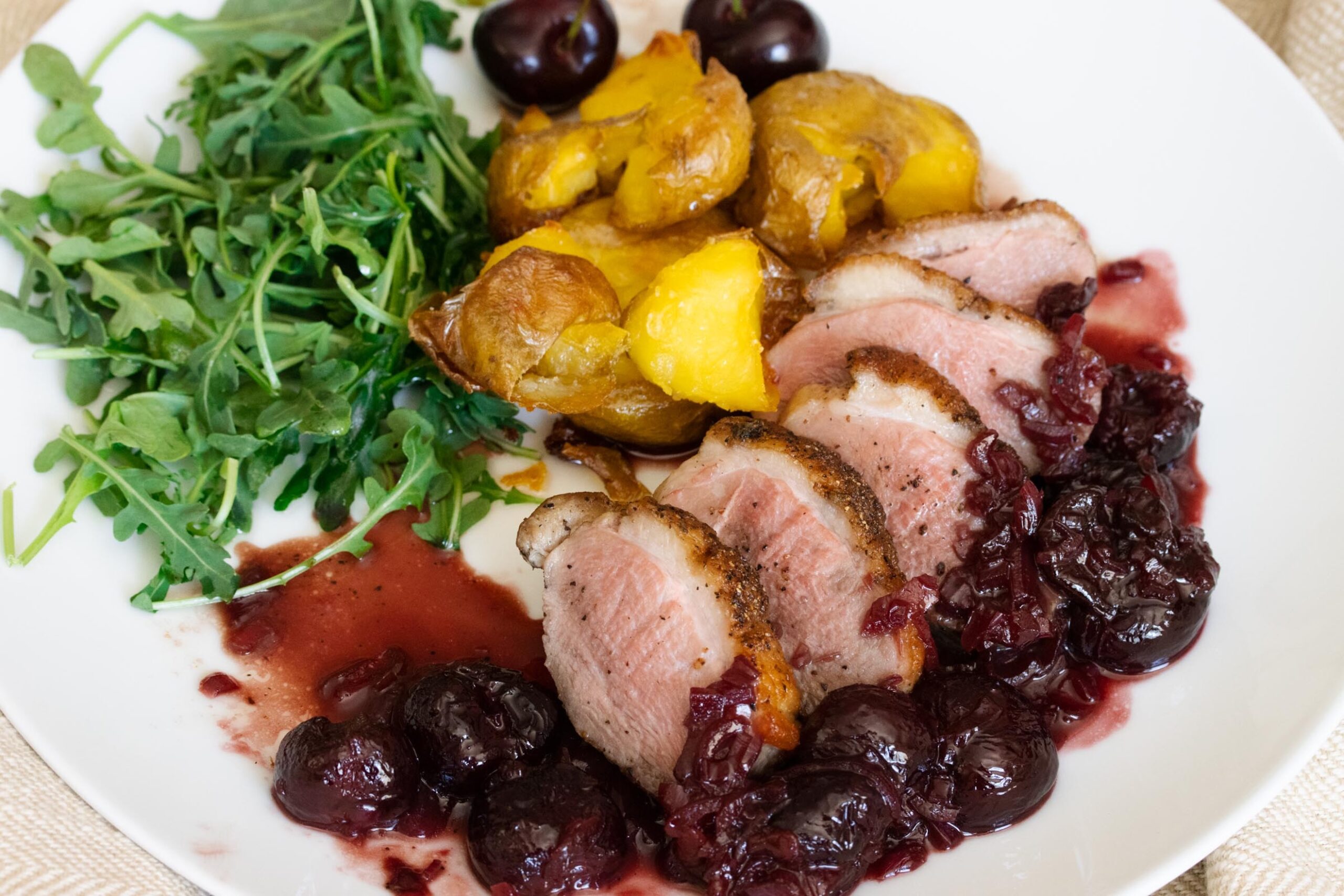 Duck Breast with Port and Cherry Sauce A plate with duck and cherry sauce with port wine reduction, potatoes and salad.