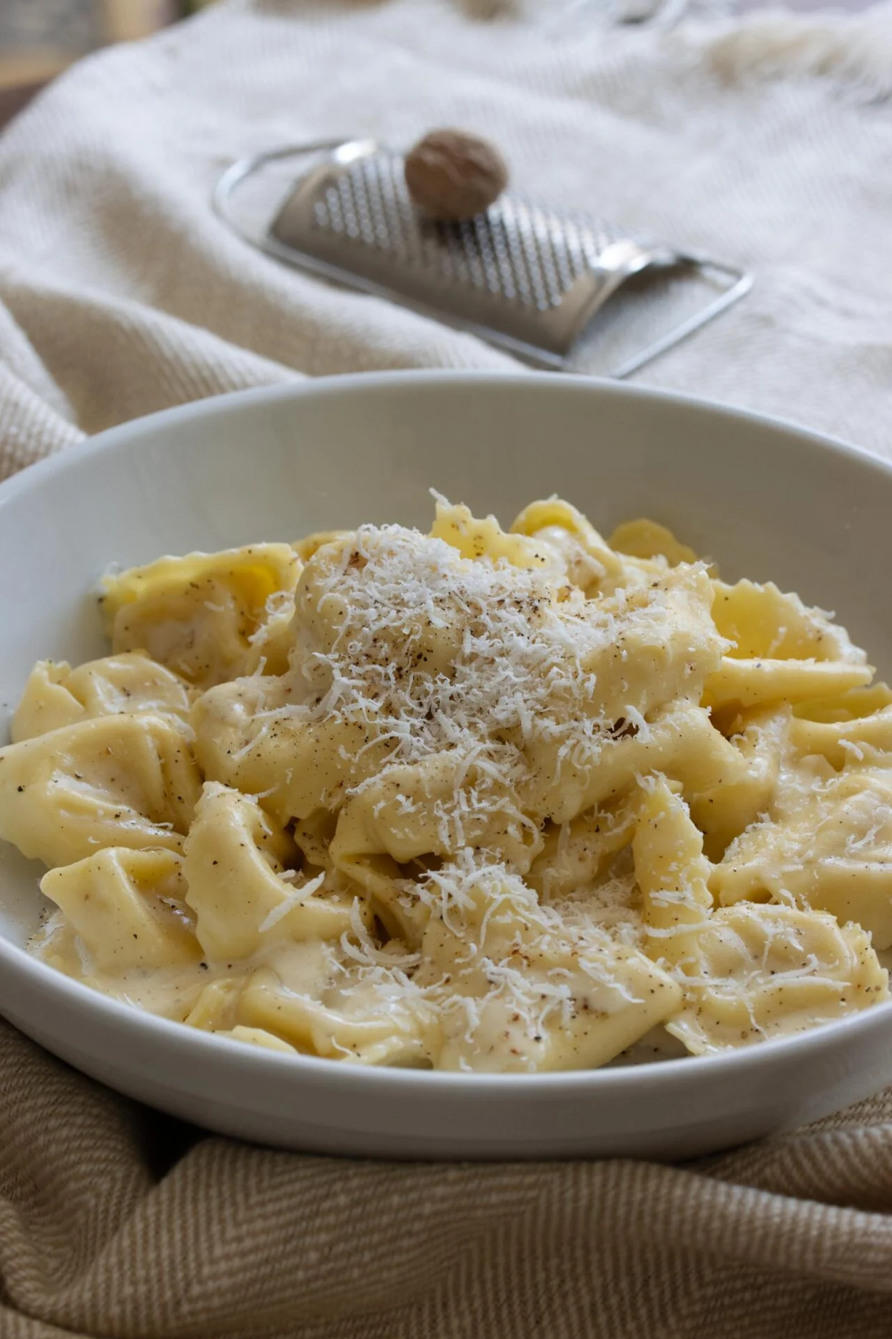 Cheese Tortellini Alfredo A bowl of tortellini on a dish towel with a grater in the background.