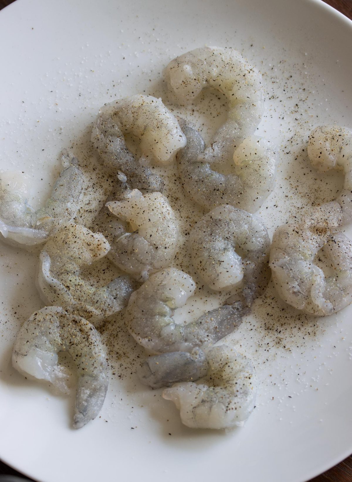 Shrimp seasoned generously wiht salt and pepper on a white plate.