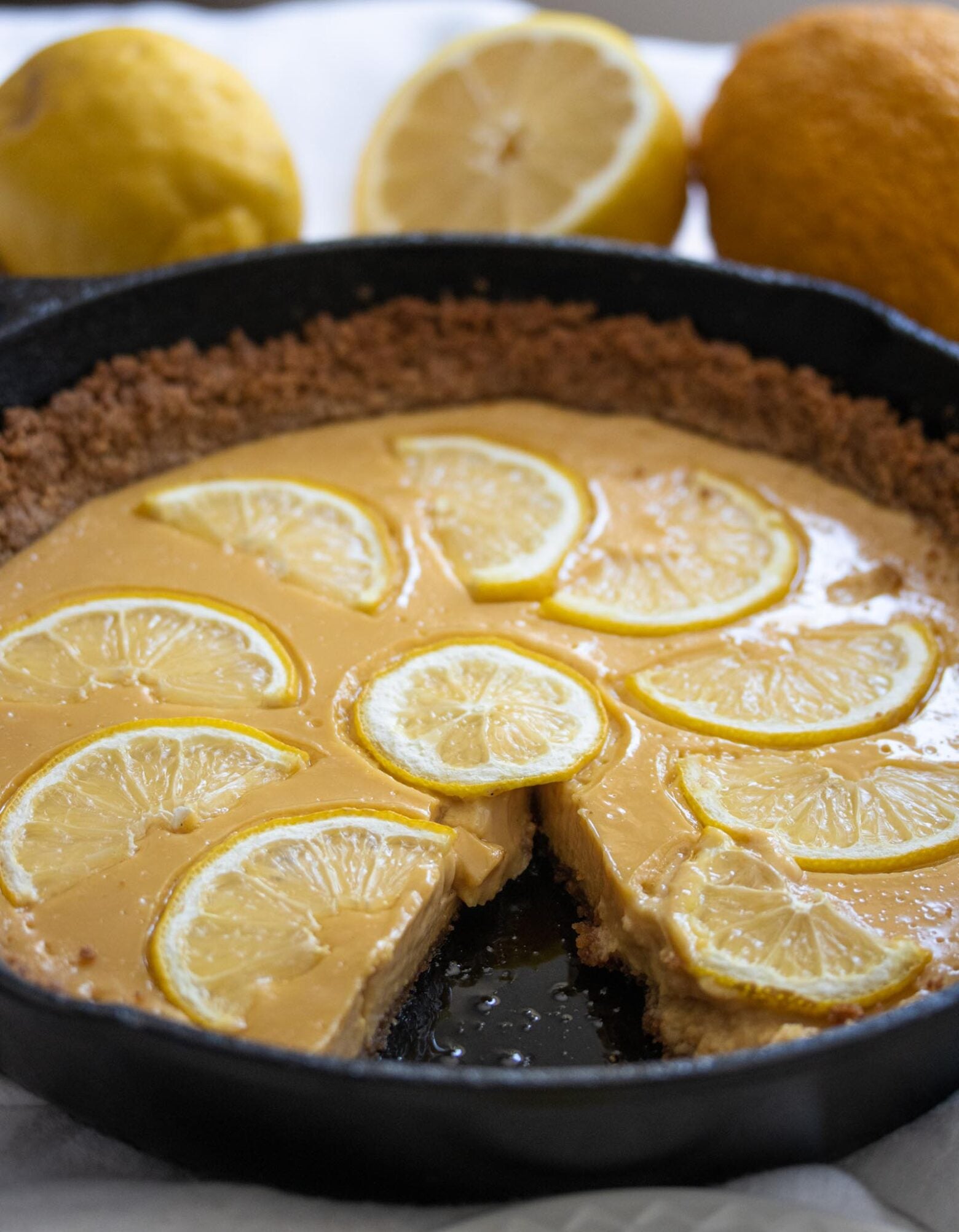 Lemon Tart A whole piece of tart in a cast iron skillet surrounded by fresh lemons.