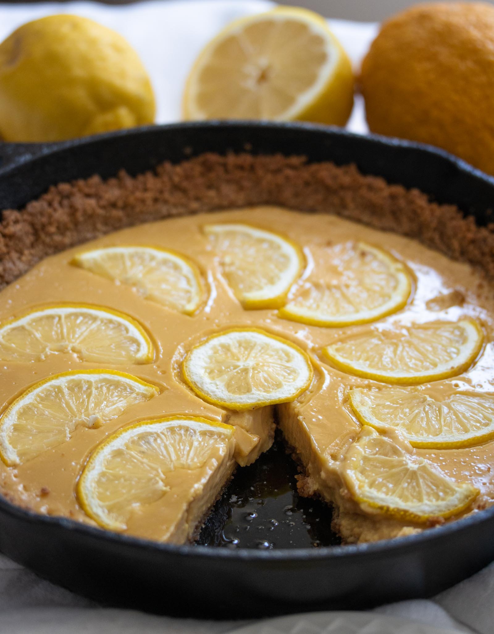 Lemon Tart A whole piece of tart in a cast iron skillet surrounded by fresh lemons.