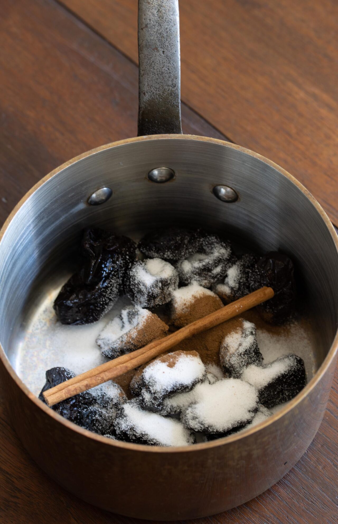 Prunes, cinnamon stick and sugar are cooked togeter in a small saucepan.