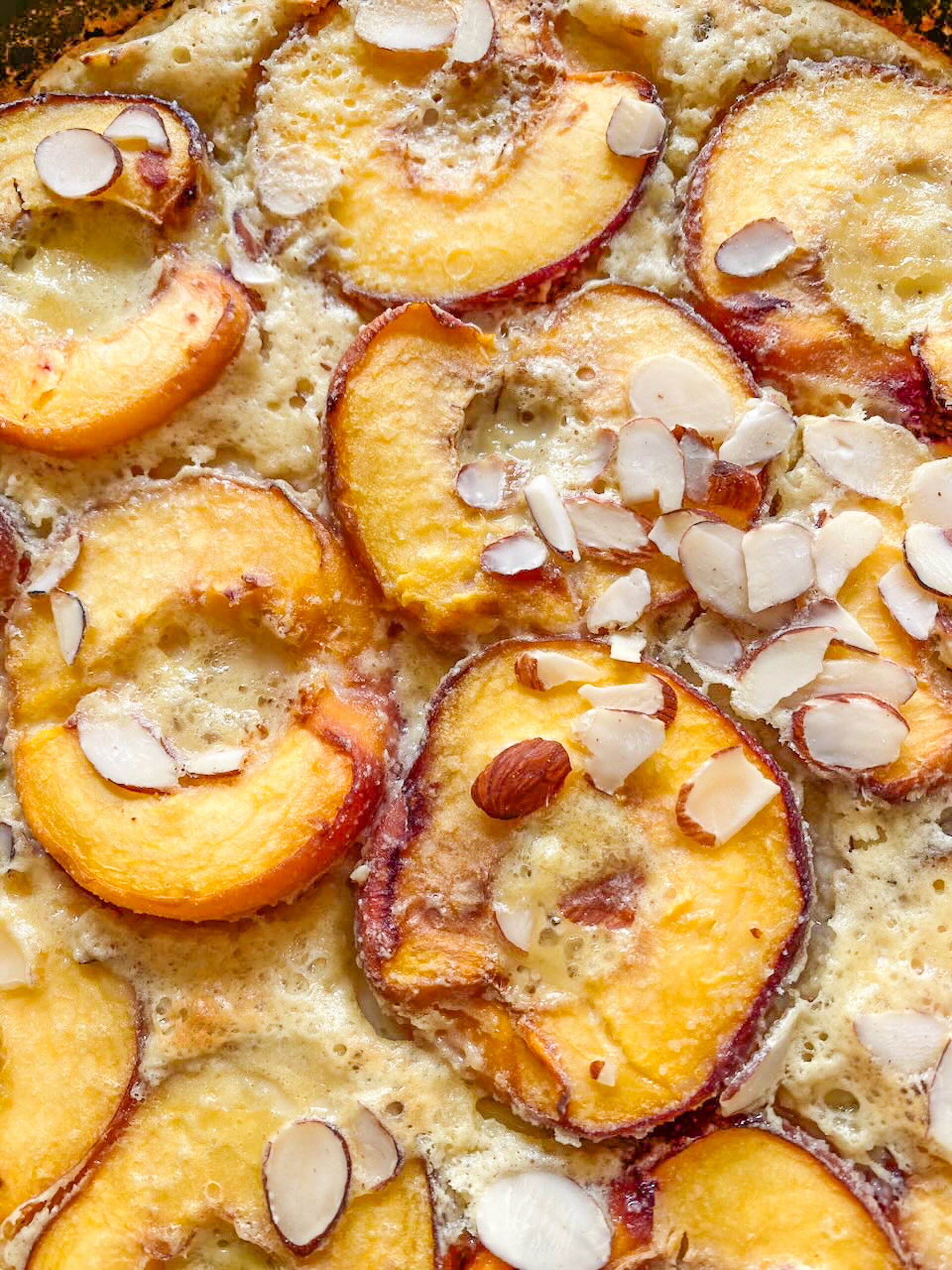 Peach Clafoutis close up after being taken out of the oven with almond slivers over it