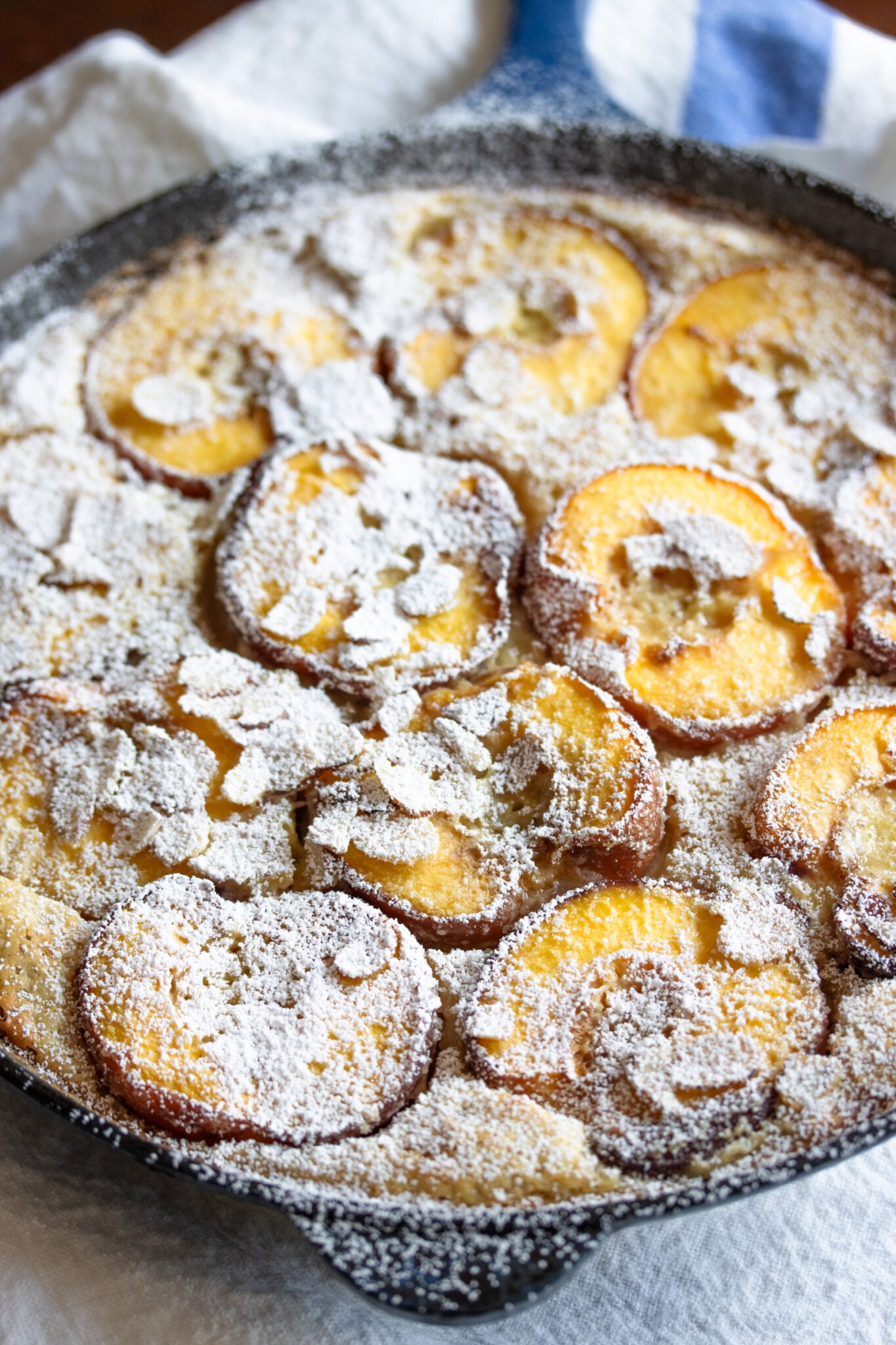 The finished peach clafoutis recipe covered in icing sugar and served in the pan.