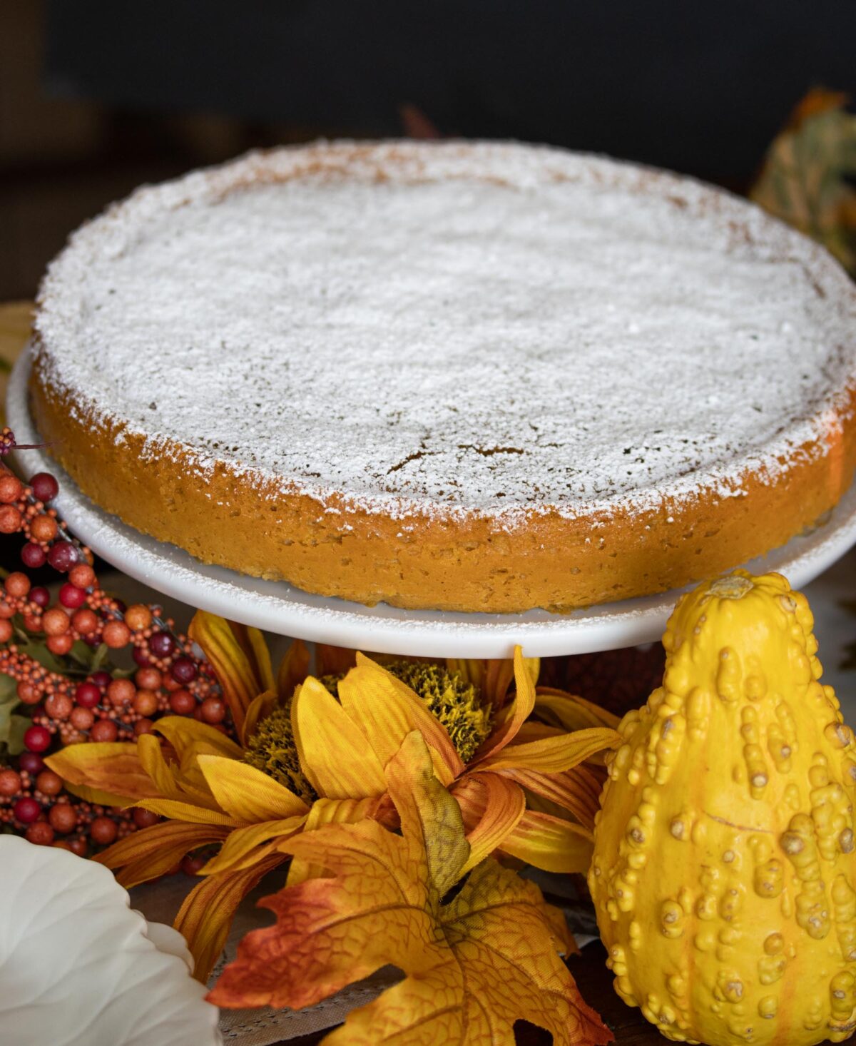 Pumpkin-White Chocolate Souffle Cake. Pumkin and white chocolate souffle cake served on a white cake stand adorned with fall foliage and gourds.