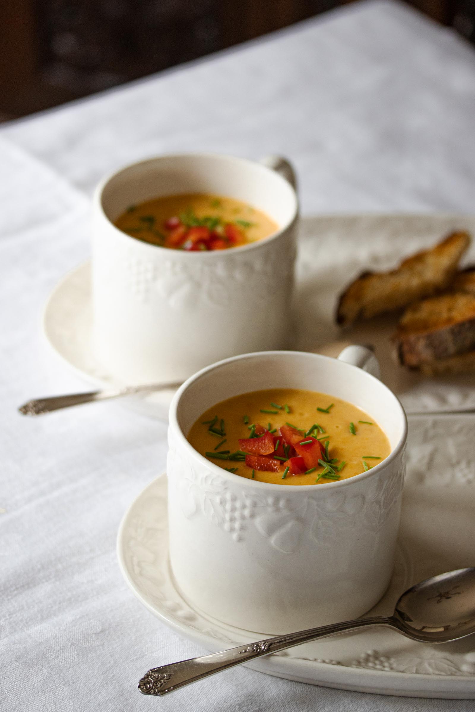 roasted bell pepper creamy soup in soup white cups wiht spoons and toasted bread